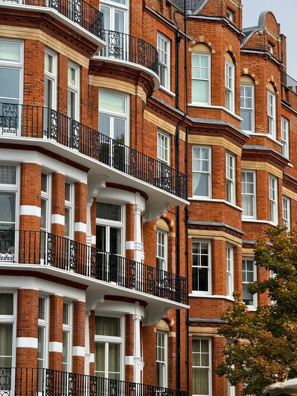 Red-brick Victorian mansion block with white stone bands and black iron balconies