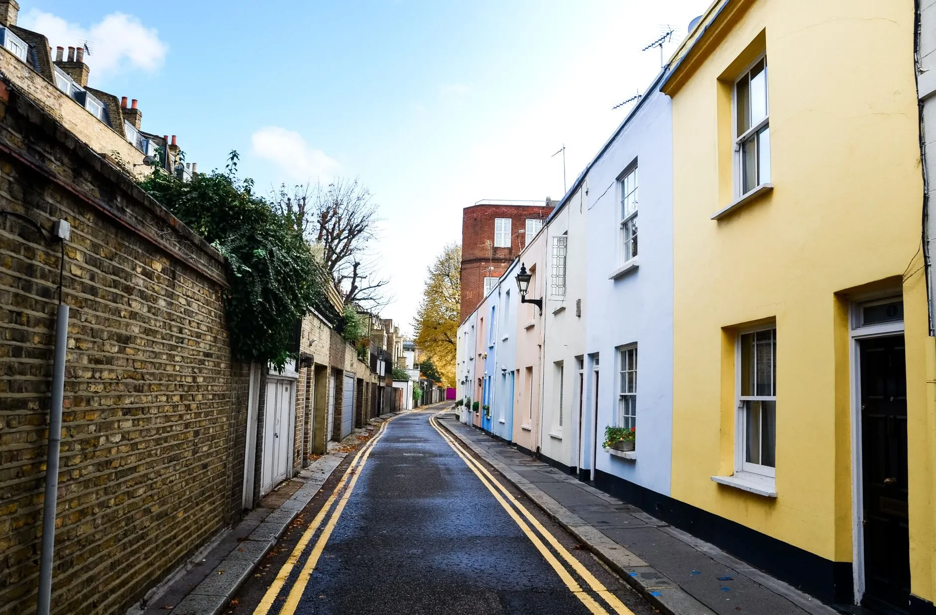 A narrow lane of painted terraced houses in yellow, white and blue beside a long brick wall